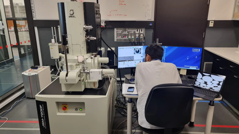Scientist operating an electron microscope while analysing material samples on a computer screen.