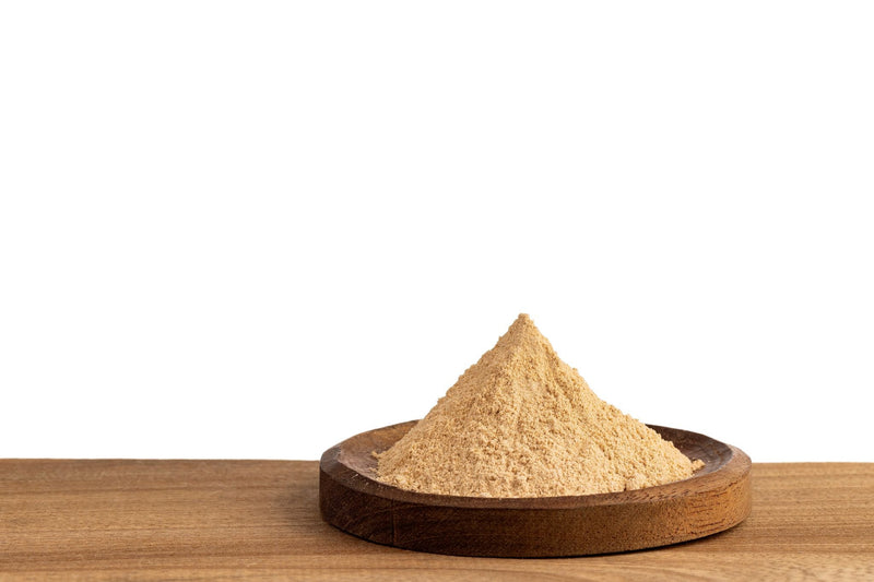 Fine Lion’s Mane mushroom powder piled on wooden dish against white background ready for supplement use