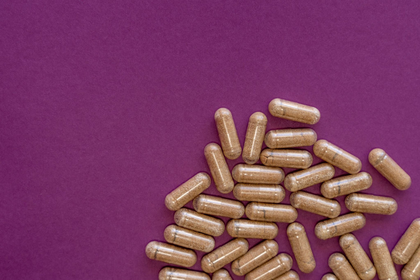 Brown mushroom extract capsules scattered on purple background in close-up flat lay composition.