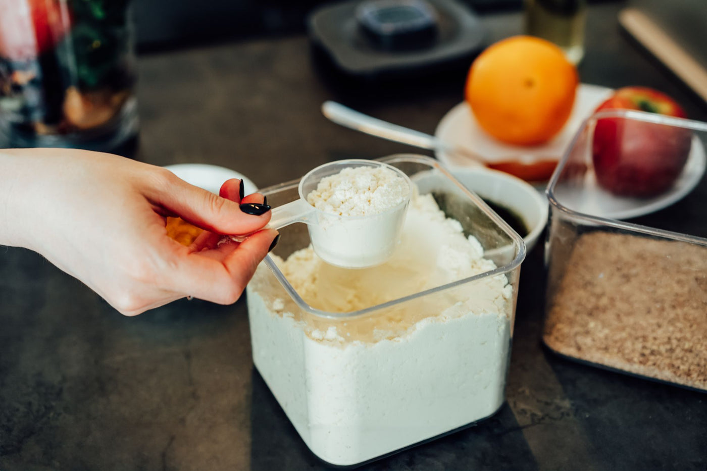 Hand scooping fine functional powder from a storage container, showing precise portioning for ready-to-mix nutrition formulations.