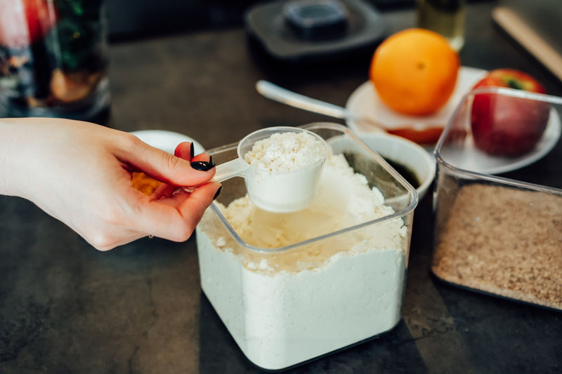Hand scooping fine functional powder from a storage container, showing precise portioning for ready-to-mix nutrition formulations.